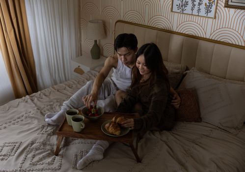 A loving couple enjoys breakfast in bed, sipping coffee in a cozy bedroom setting.