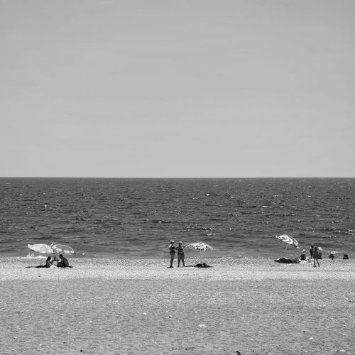 Free A serene black and white photo of a beach with people relaxing and umbrellas by the sea. Stock Photo