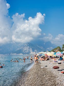 Vacationers enjoy a sunny day on a crowded pebble beach by the ocean.