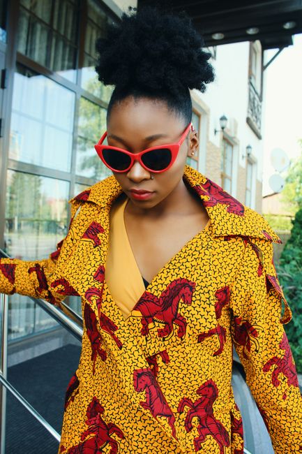 Fashionable African woman wearing colorful attire and red sunglasses outdoors.