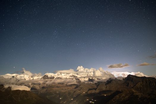 Star-filled sky over snowy mountains and clouds at night. Scenic and serene view.
