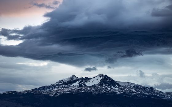 Capture of storm clouds gathering over snow-covered mountains, creating a dramatic landscape scene.