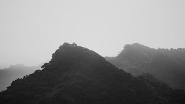 A tranquil black and white photograph of a mountain peak with a temple, shrouded in mist.