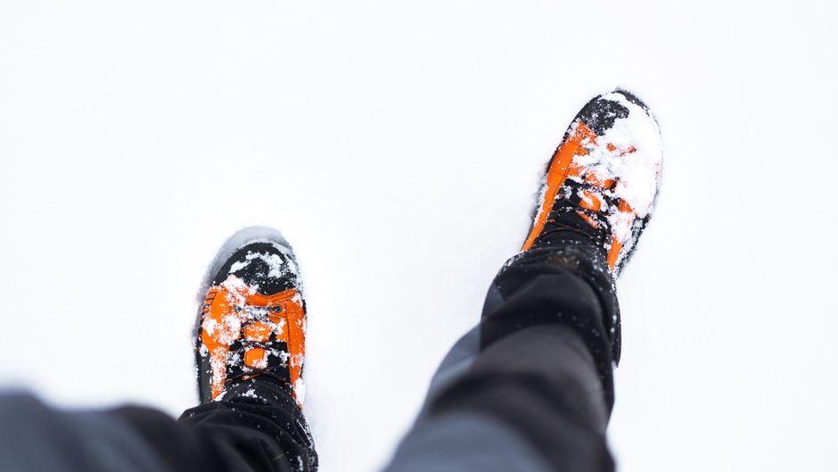 Orange winter boots covered in snow, viewed from above, on a snowy day.