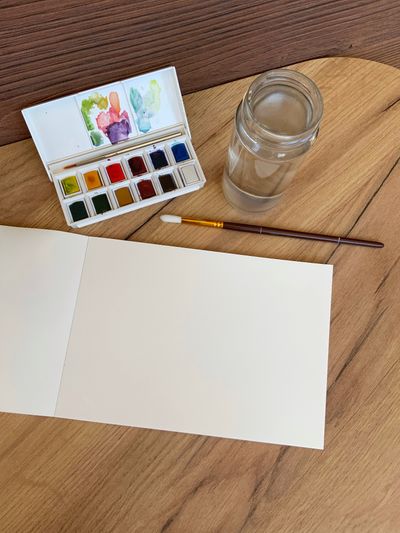 Watercolour pan set, brush and blank paper on a wooden desk — photo by Marharyta Shtyfura on Pexels