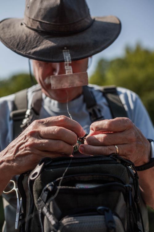 Free An adult man organizing his fishing equipment while wearing a hat outdoors. Stock Photo