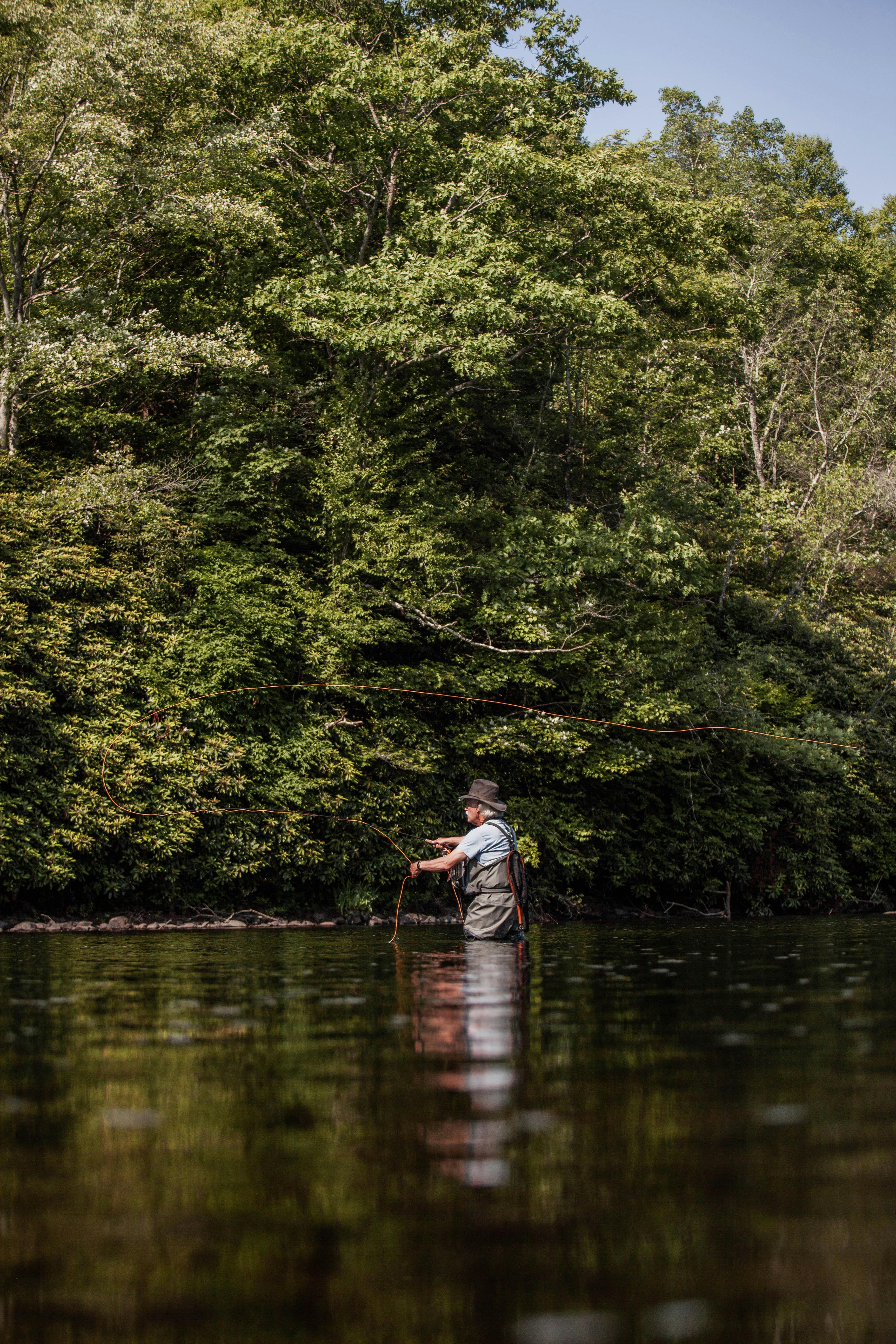 An adult man fly fishing in a calm forest river during a sunny summer day.