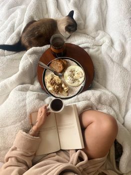 A warm and cozy morning featuring breakfast, a book, and a cat.