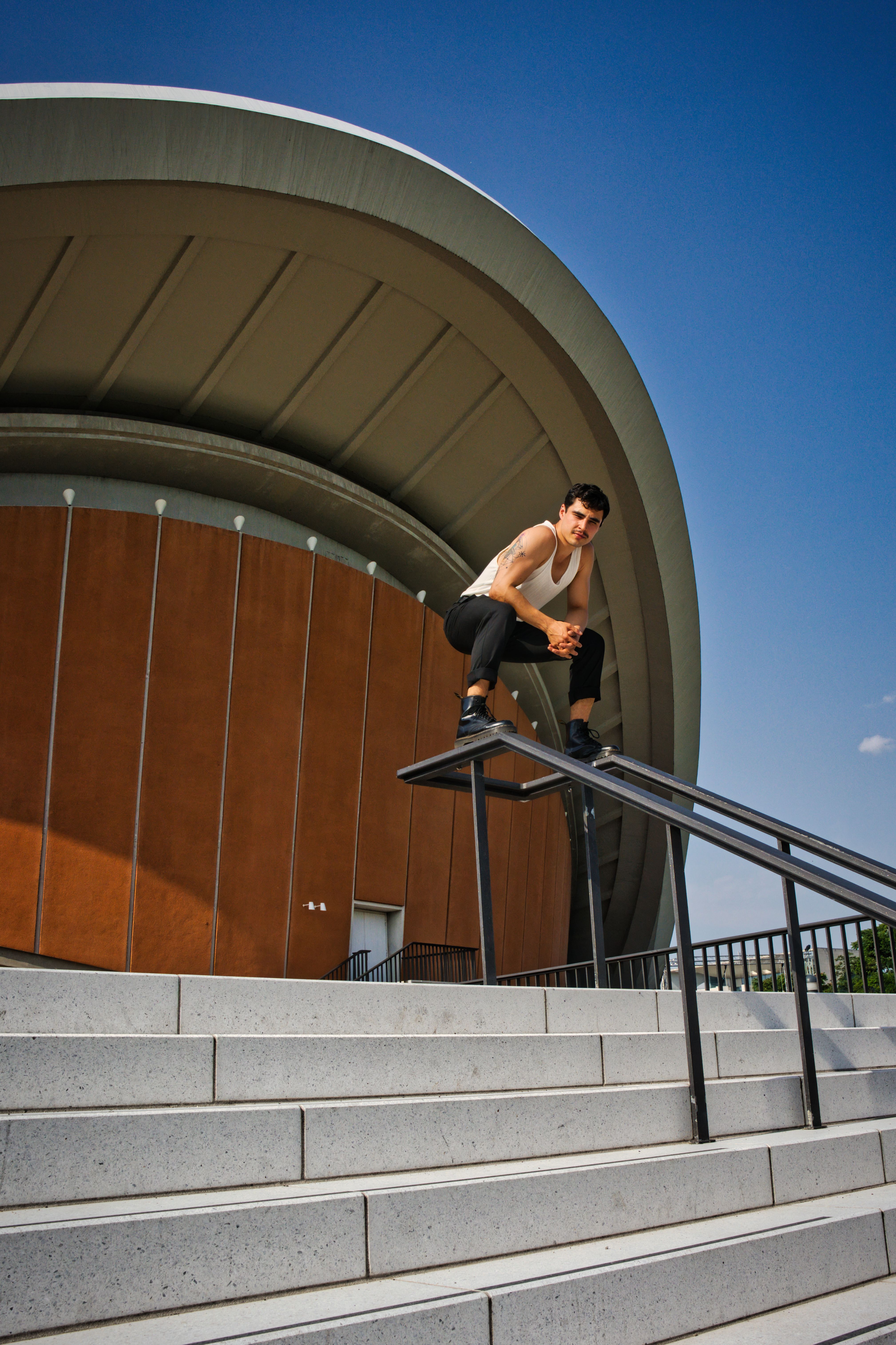Man posing on handrail with urban architecture background in Berlin.