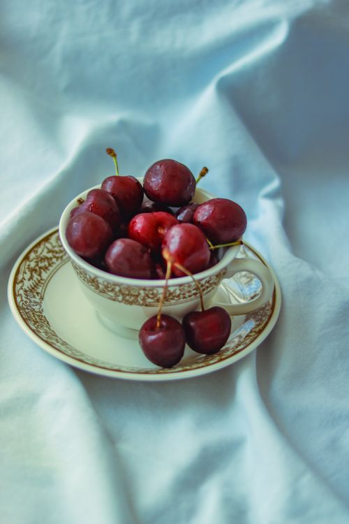 Free A collection of ripe cherries beautifully arranged in a porcelain cup on a soft fabric. Stock Photo