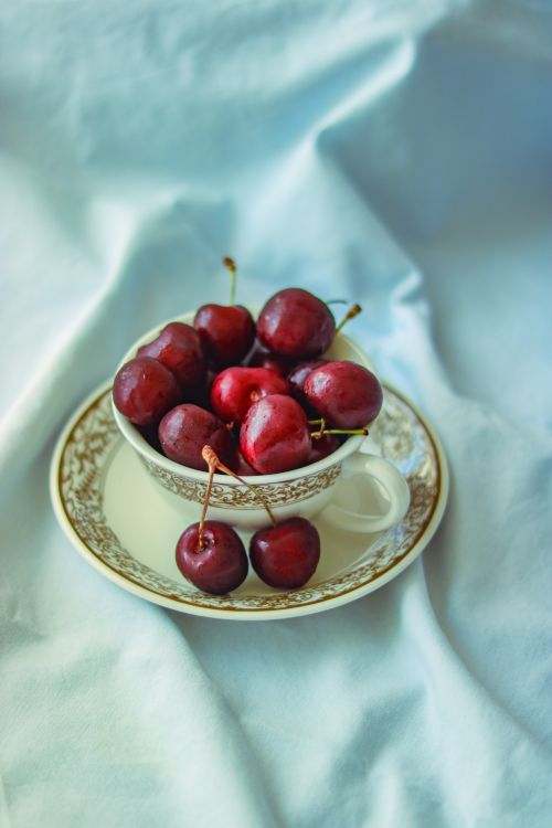 Free A close-up of ripe red cherries in a vintage porcelain cup on a soft fabric background. Stock Photo