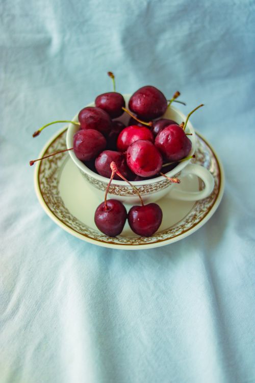Free A classic teacup overflowing with ripe red cherries on a saucer, symbolizing freshness. Stock Photo