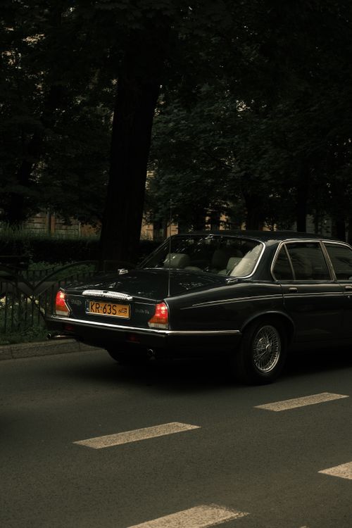Free A classic black car drives down a city street, showcasing vintage automotive design. Stock Photo
