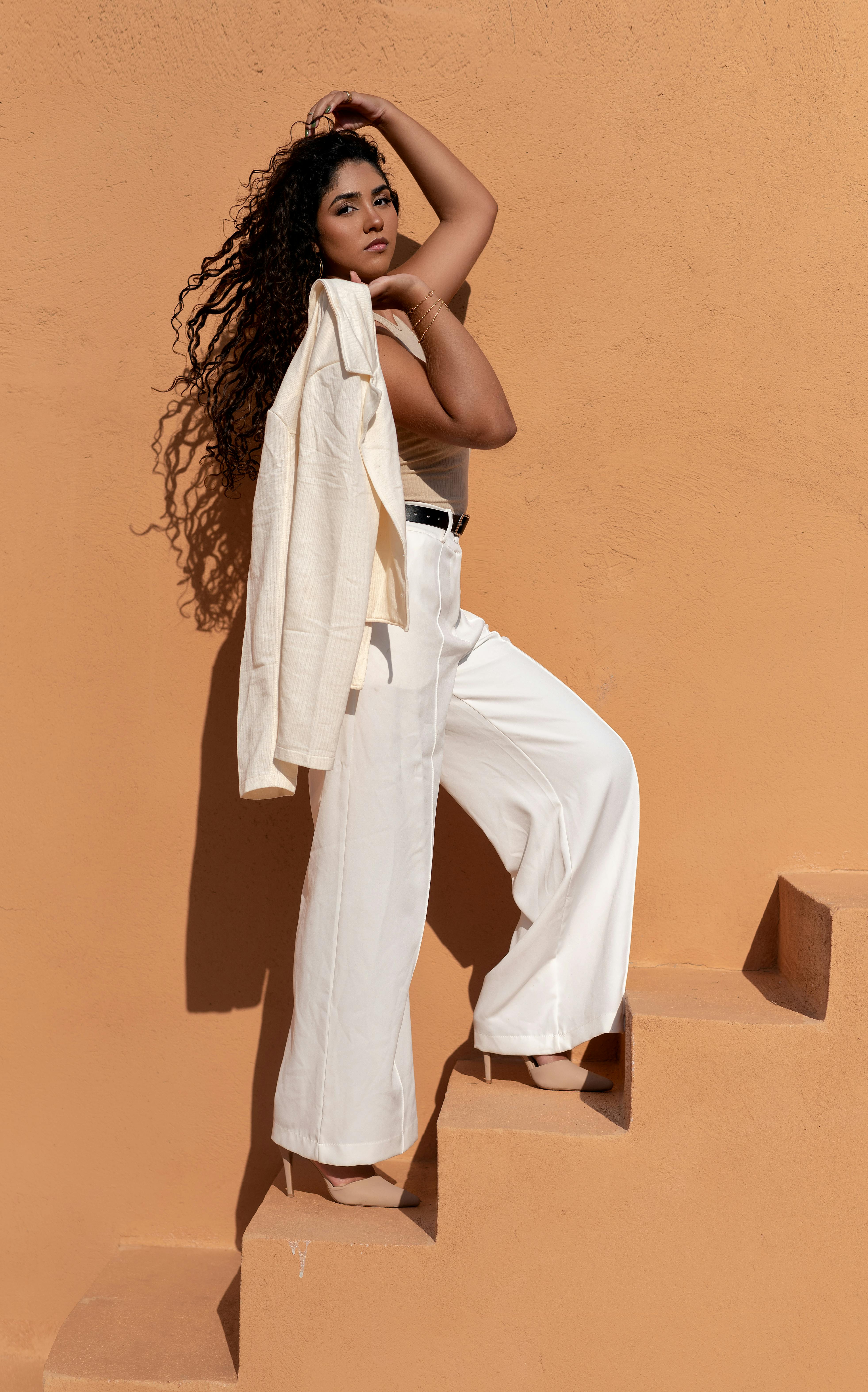 Fashionable woman poses in white outfit on outdoor steps, showcasing style.