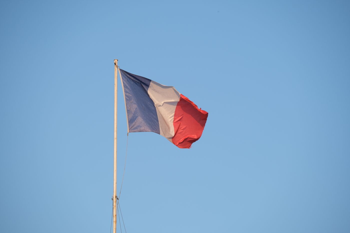 Un drapeau français bleu, blanc et rouge flotte devant un ciel bleu.