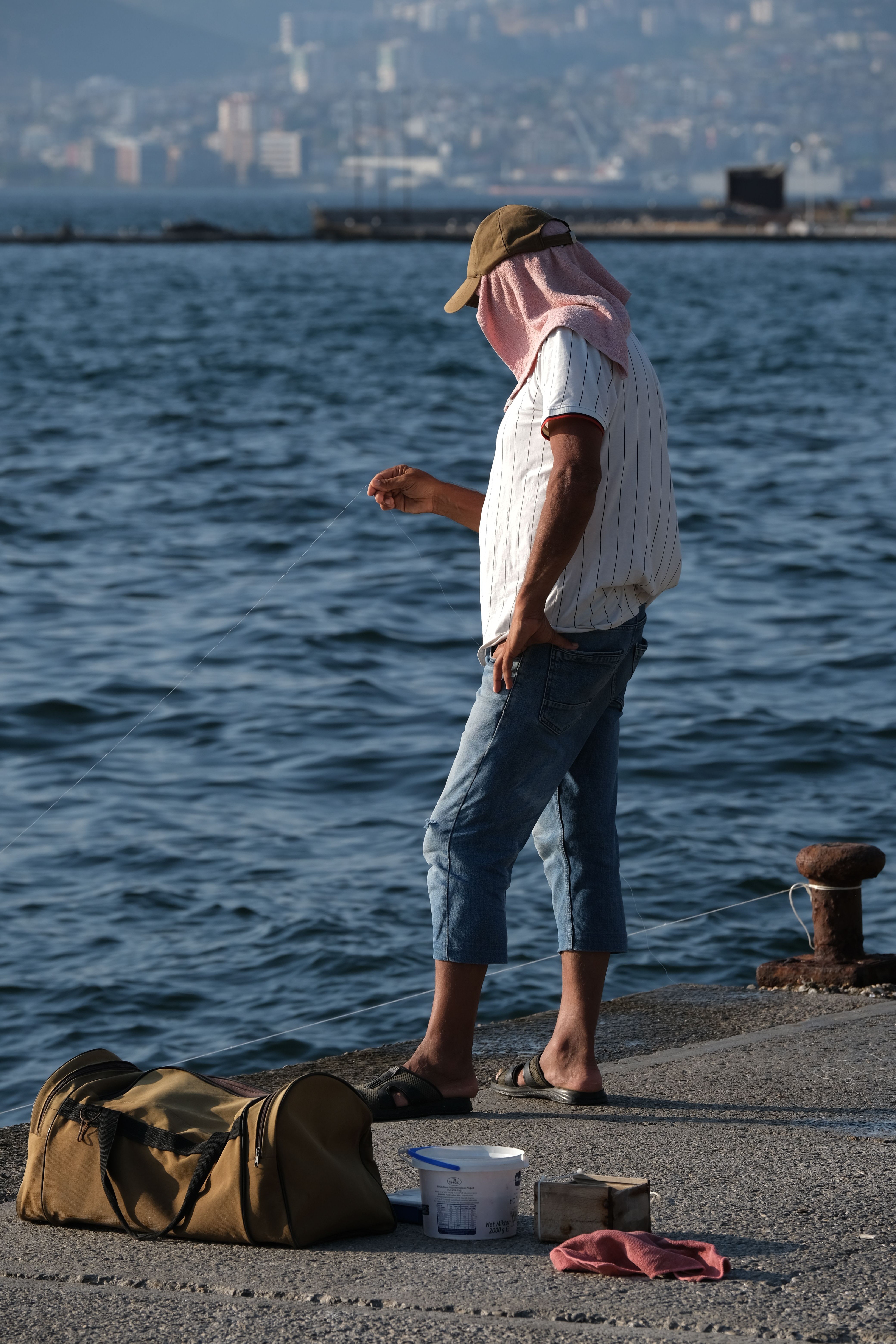 A fisherman stands by İzmir shore with fishing gear, capturing the essence of seaside angling.