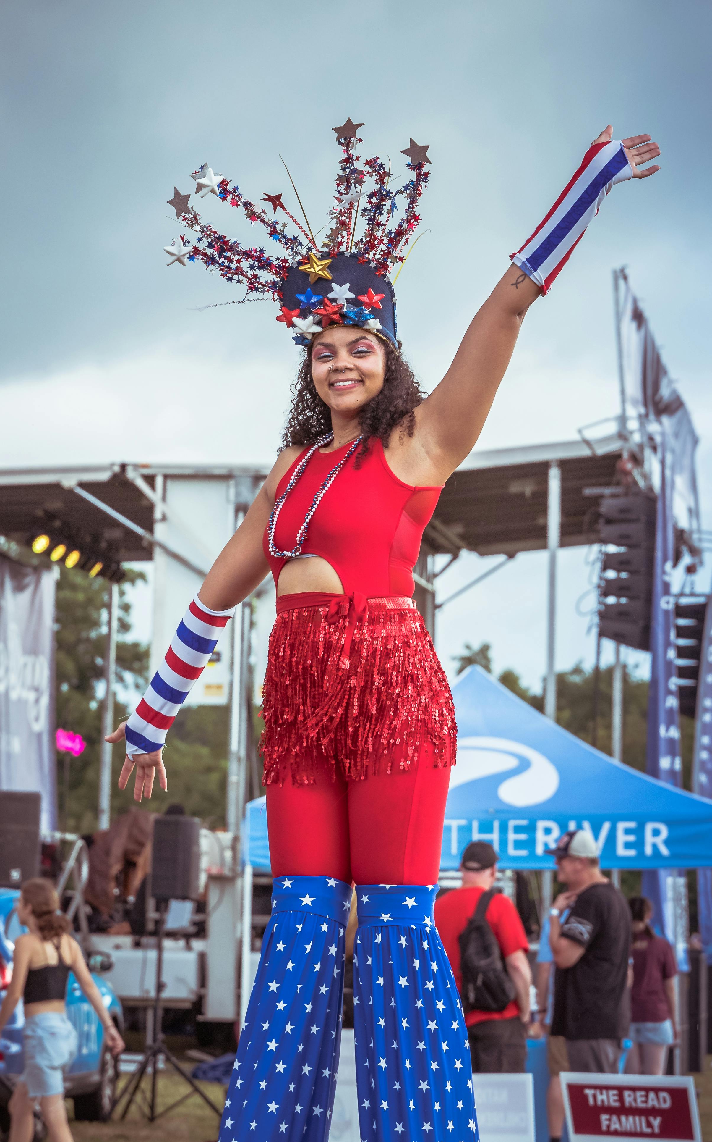 A smiling performer wearing a patriotic costume and stilts entertains at an outdoor festival.