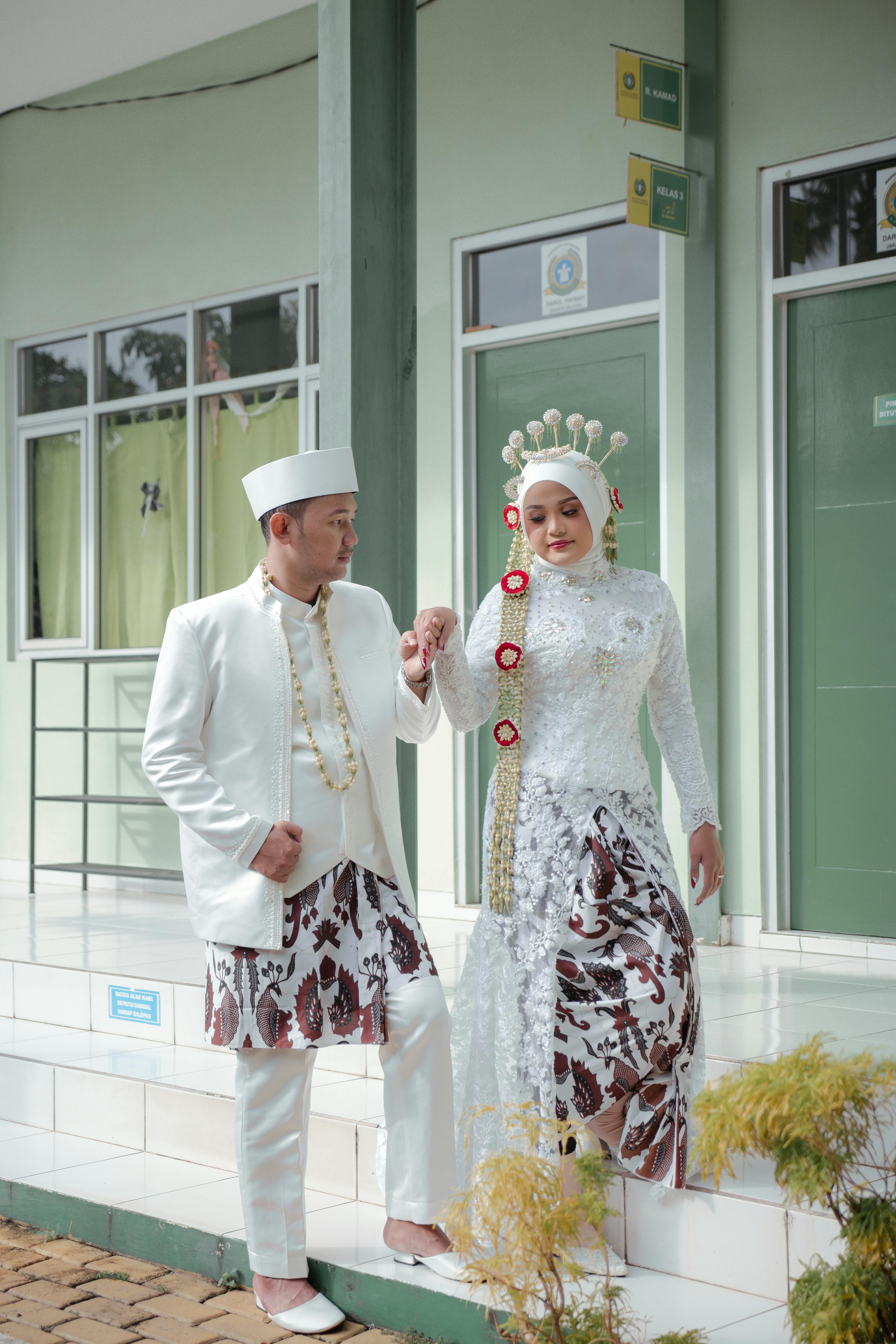 Couple in elegant Indonesian traditional wedding clothing outdoors.