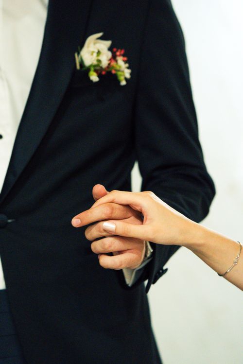 Free Close-up of a newlywed couple holding hands, showcasing a wedding suit and floral details. Stock Photo