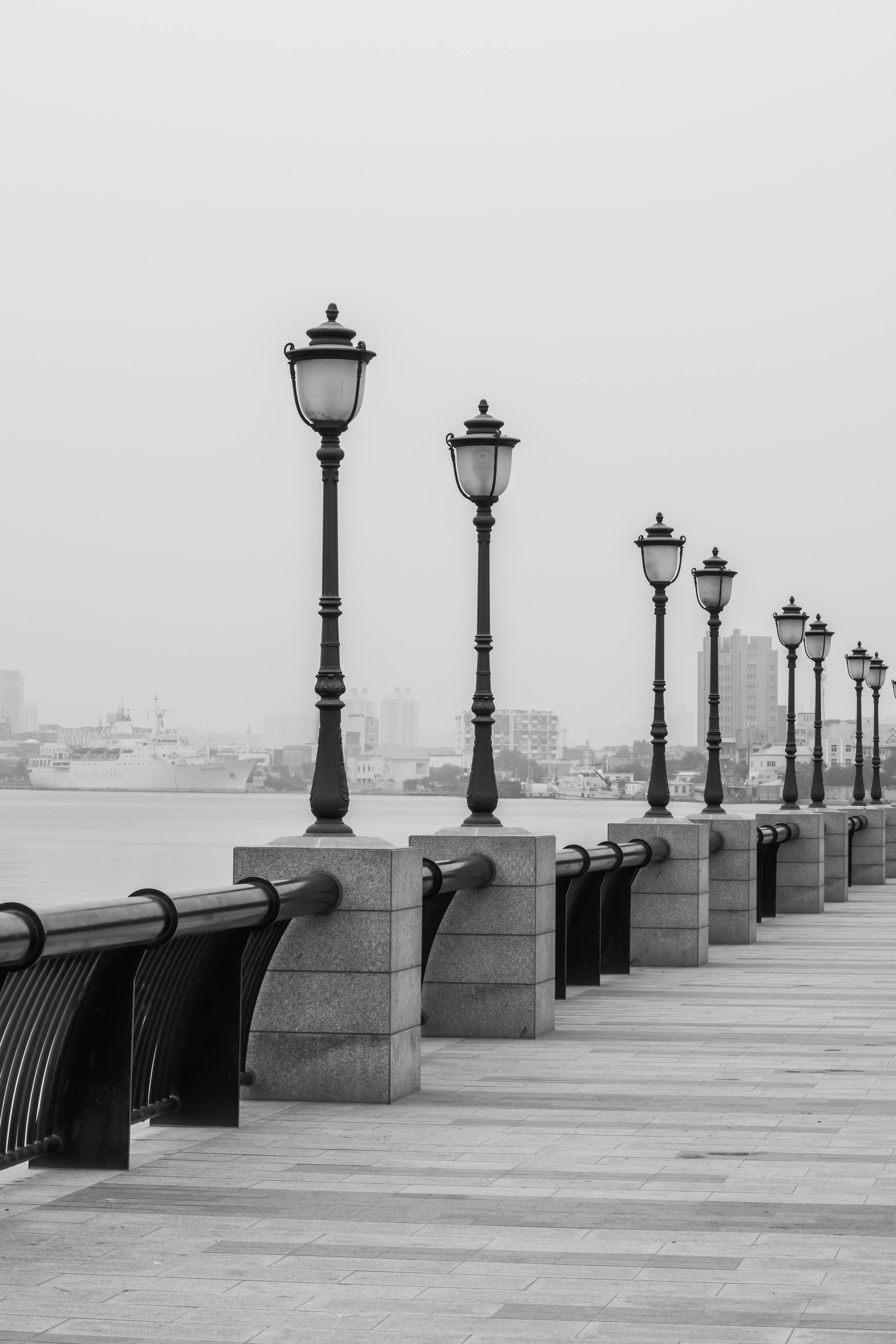Foggy urban pier with classic lanterns lining the seashore, creating a serene and timeless atmosphere.