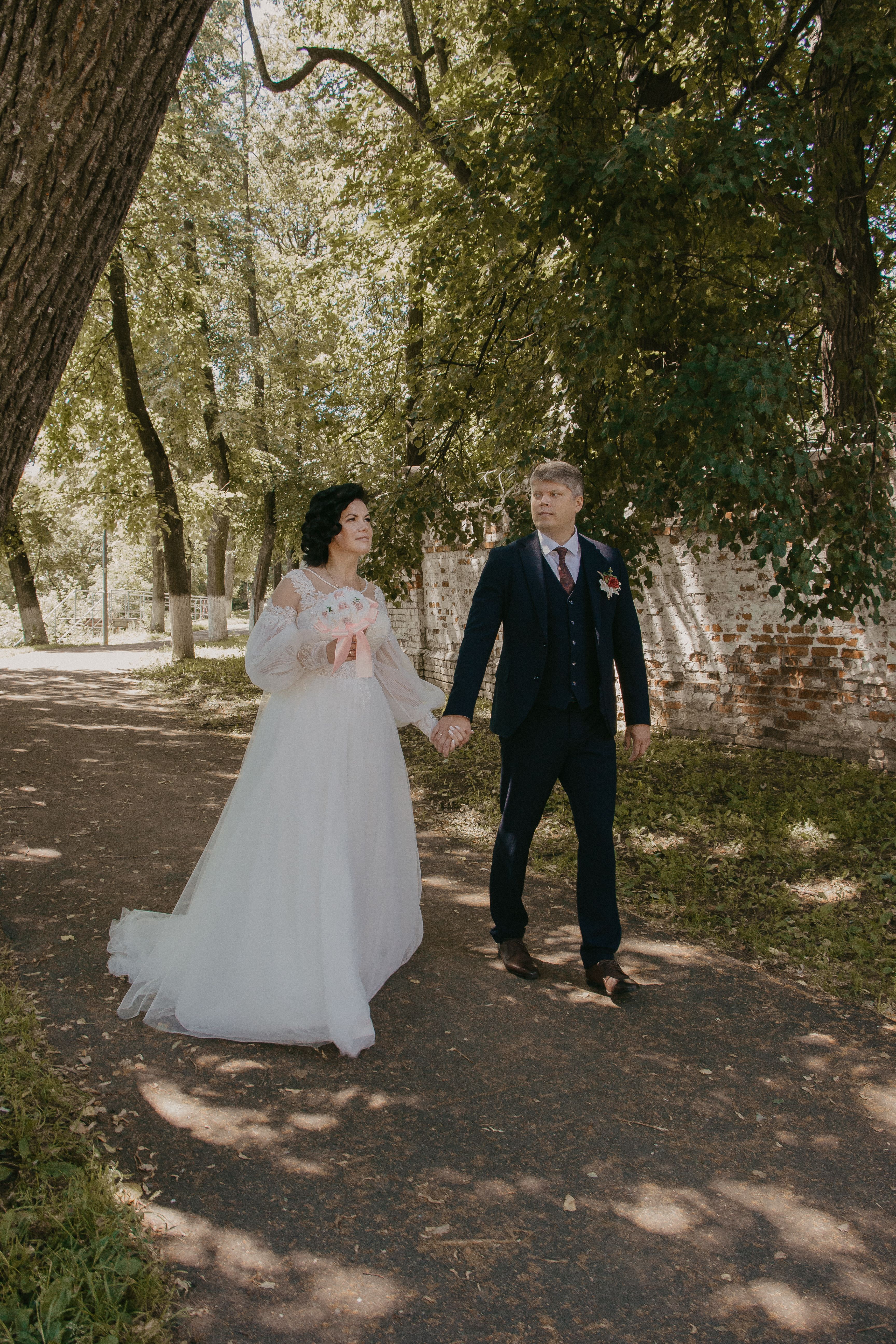 Smiling Wedding Couple Holding Hands Walking in Park · Free Stock Photo