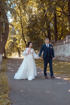 Newlywed couple walking hand in hand in a scenic park under sunlight.