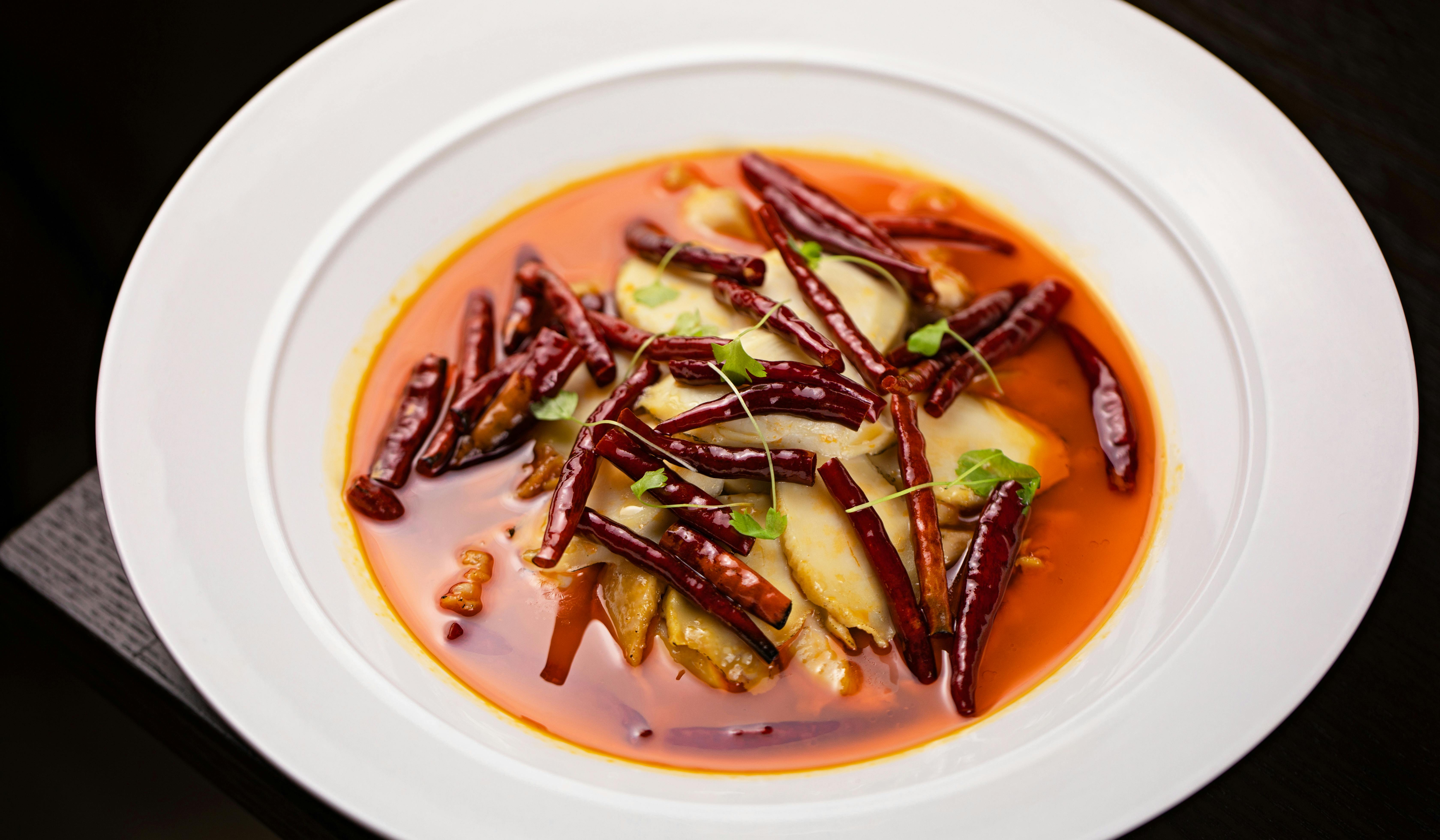 A bowl of tender white fish fillets and vegetables glistening in glossy red chili oil, topped with fresh sliced scallions and bright cilantro leaves