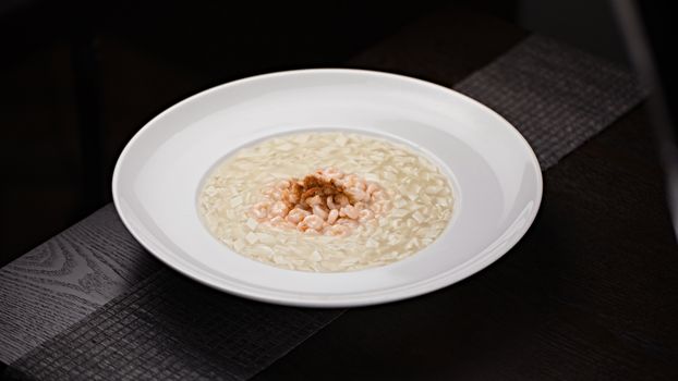 A close-up of a creamy risotto topped with shrimp, elegantly served on a white plate.