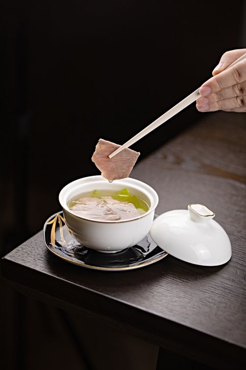 Free A close-up of a gourmet Asian soup with chopsticks picking up tender meat in an elegant setting. Stock Photo