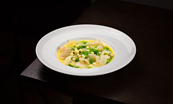 A beautifully presented gourmet soup with fresh vegetables in a white bowl on a dark background.