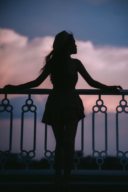 Silhouette of a woman looking at the sunset, framed by a decorative railing.