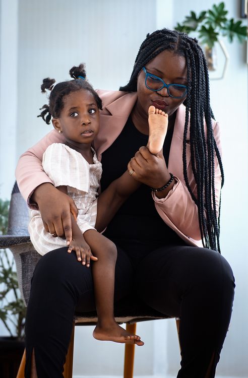 Free A woman with braids holds her daughter affectionately on her lap inside a cozy home. Stock Photo