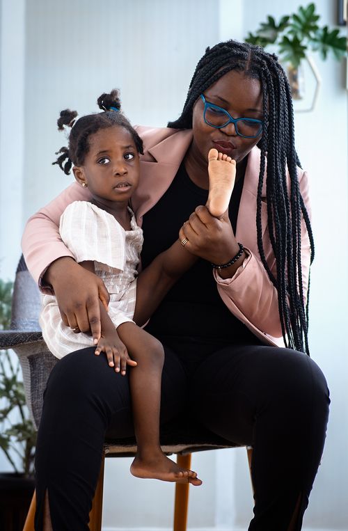 Free A woman with braids holds her daughter affectionately on her lap inside a cozy home. Stock Photo