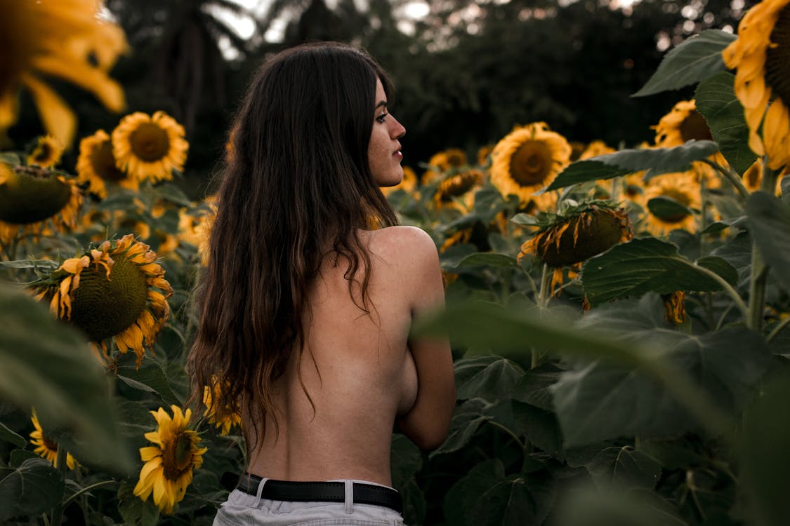 shirtless woman sorrounded by sunflowers