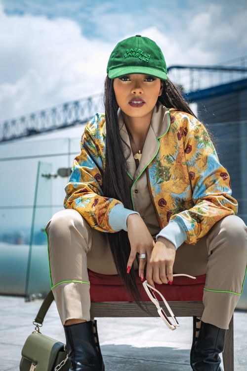 Free A stylish woman in a colorful jacket and green cap poses confidently on a rooftop in Mexico City. Stock Photo