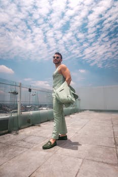 Man in green suit and sunglasses poses on rooftop in Mexico City under a bright sky.
