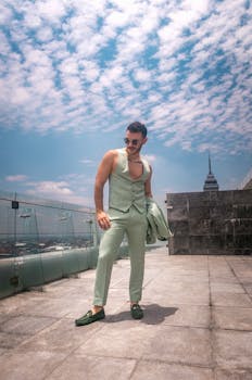 Fashionable man in sunglasses posing on a rooftop in Mexico City with a skyscraper view.