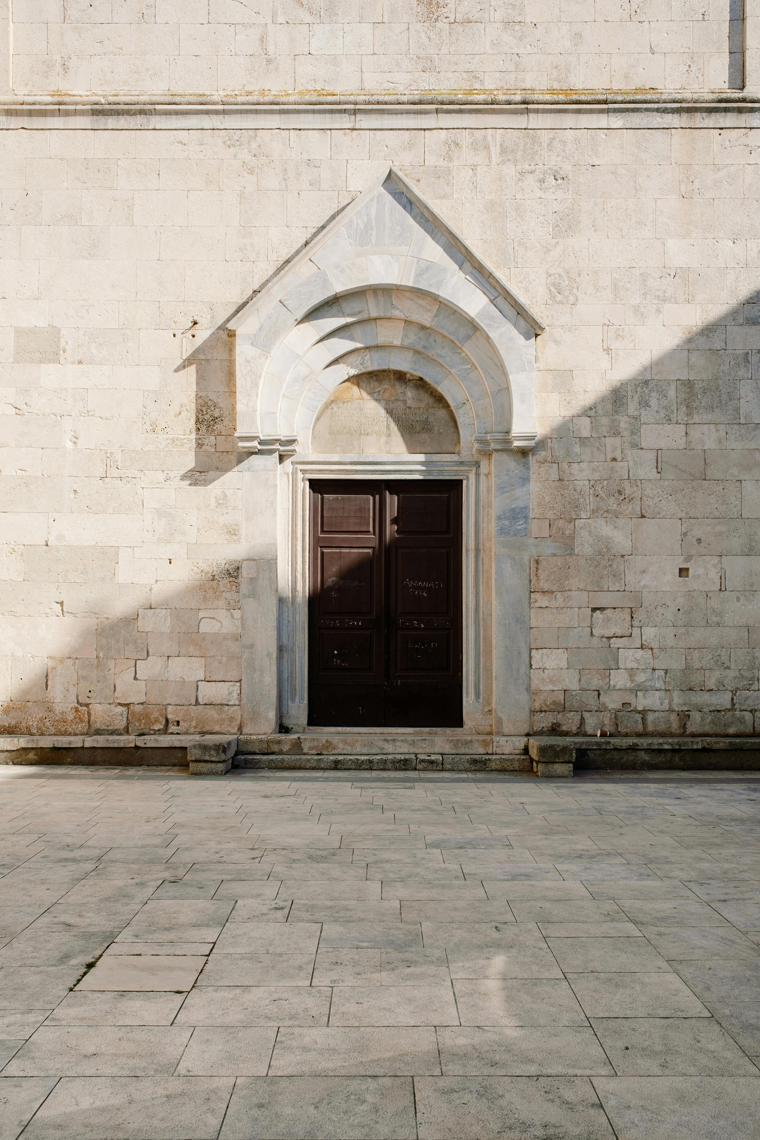 Capture of a classical stone building facade with a wooden door and arched doorway.