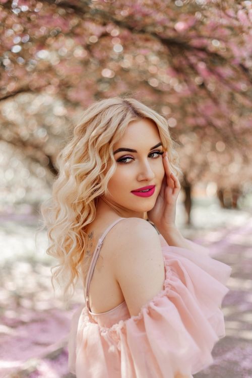 Free Elegant portrait of a blonde woman in a pink dress among blooming cherry blossoms, embodying spring beauty. Stock Photo