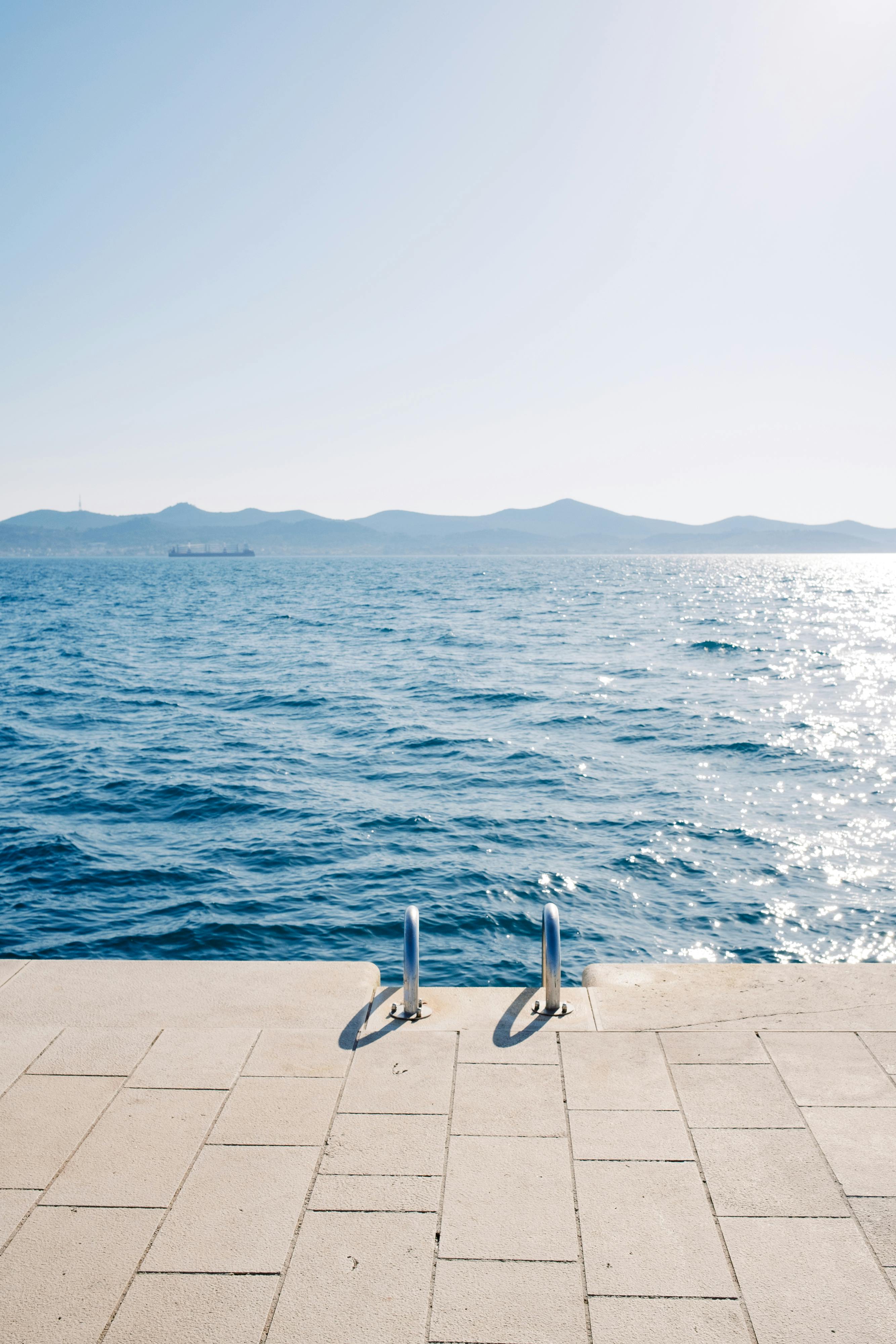 Serene oceanscape with clear blue water and distant mountains under a bright clear sky.