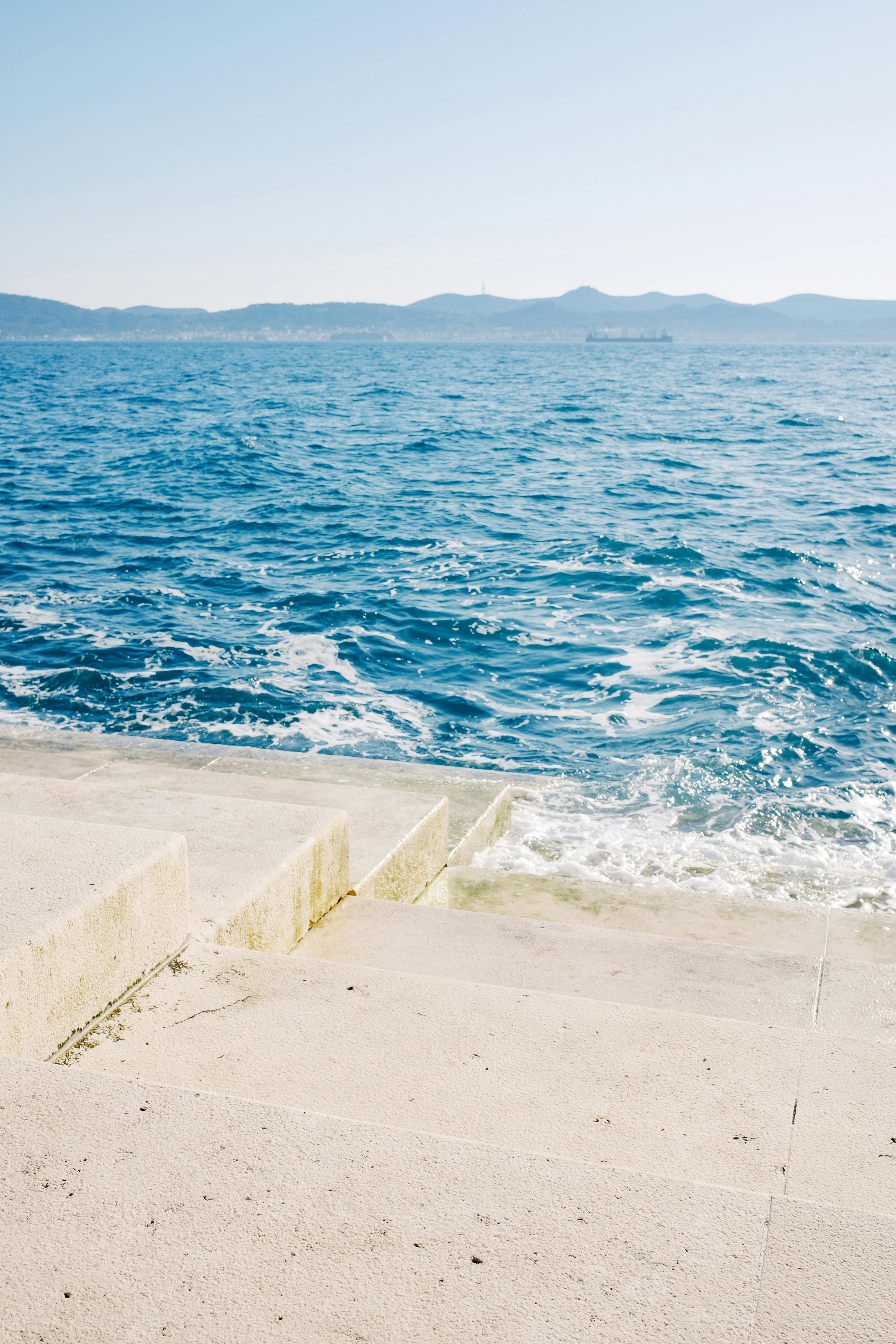 Calm ocean waves at the horizon with stone steps leading to the water in a tranquil landscape.