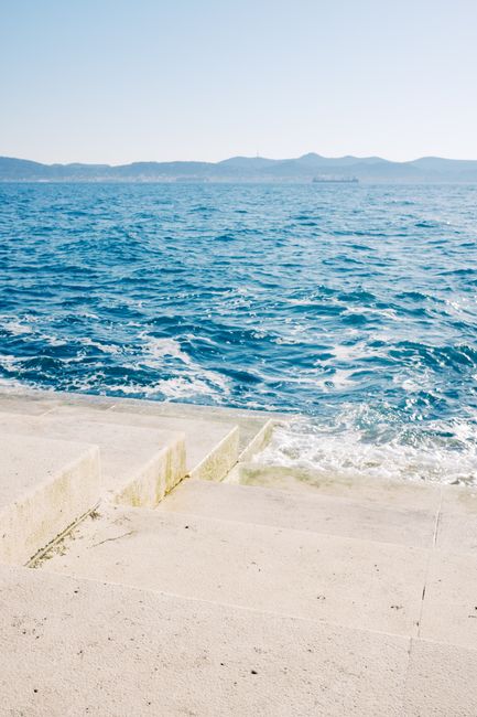 Calm ocean waves at the horizon with stone steps leading to the water in a tranquil landscape.