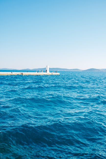 Peaceful view of a lighthouse on a pier surrounded by the vast ocean under a clear blue sky.