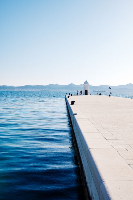 A serene view of a pier leading to a lighthouse with a tranquil ocean backdrop.