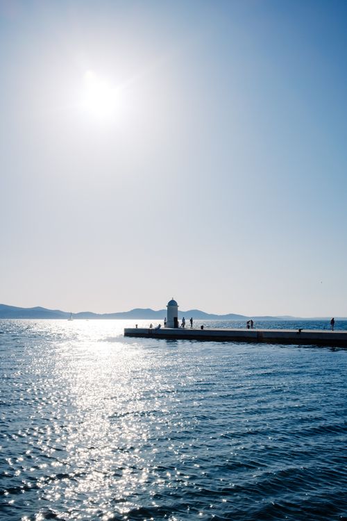 Free Lighthouse on a pier overlooking the ocean under a clear blue sky and bright sun. Stock Photo