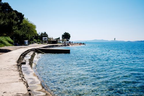 Free Explore a tranquil coastal pathway with clear blue waters under a bright sky, ideal for leisurely walks. Stock Photo
