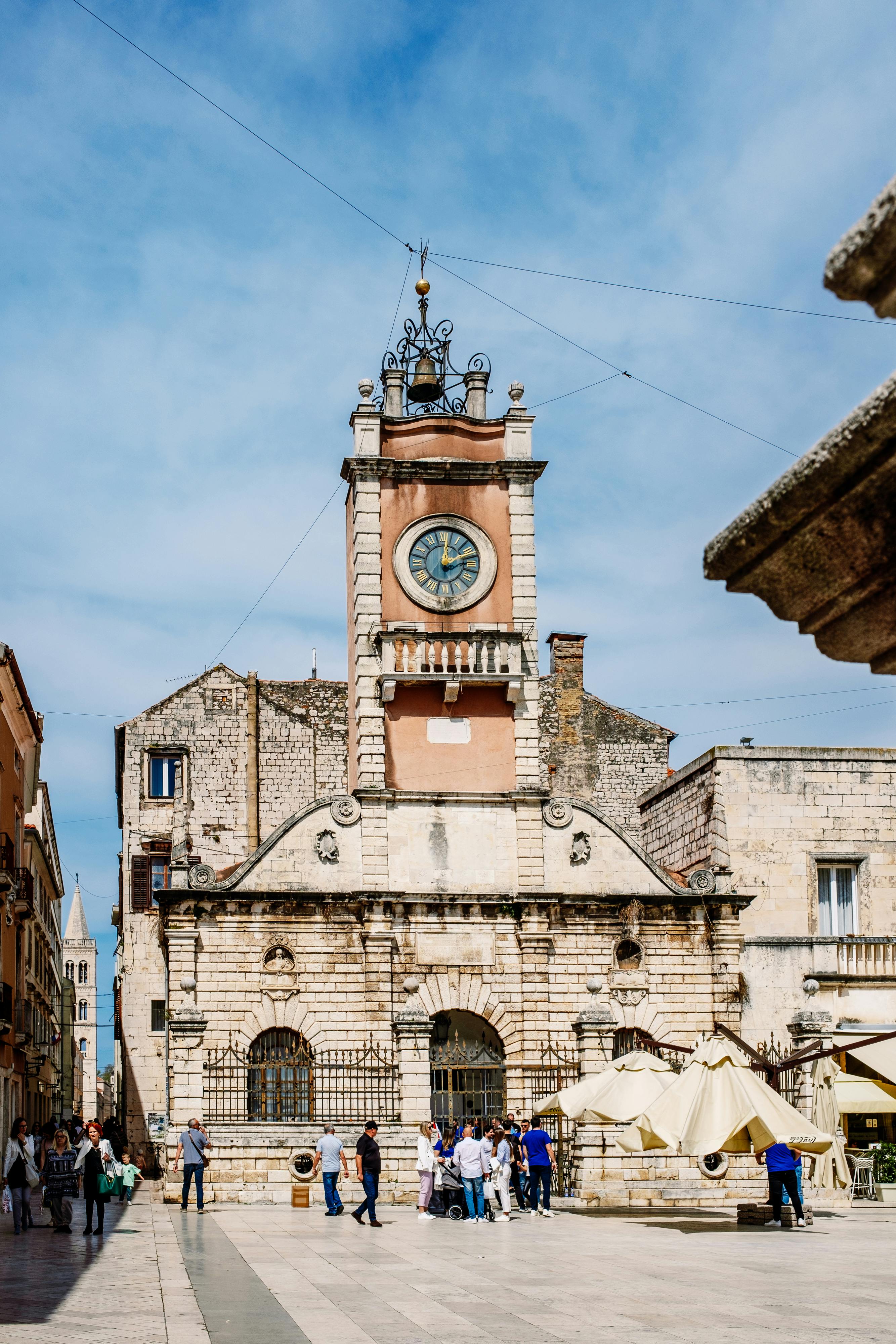 A clock tower in a square with people walking around