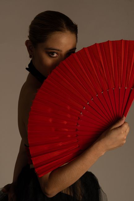 Stunning portrait of a woman partially concealed by a vibrant red fan, exuding elegance.