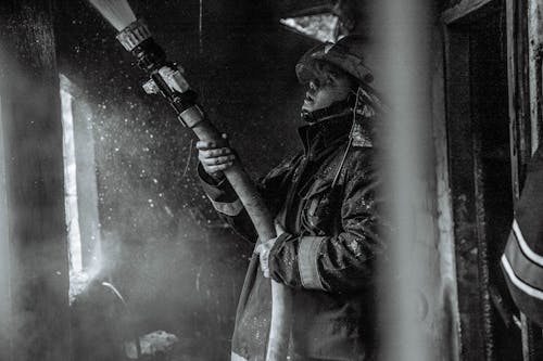 Grayscale Photography of a Fireman Holding a Hose