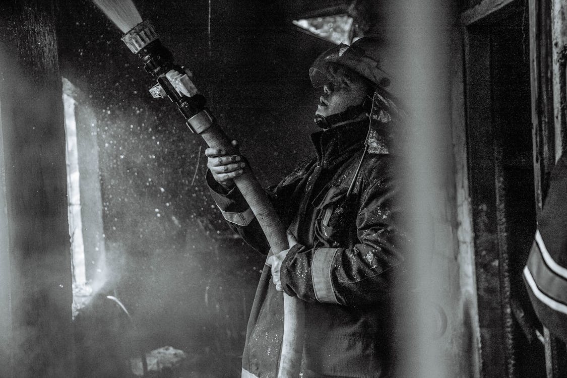 Free Grayscale Photography of a Fireman Holding a Hose Stock Photo